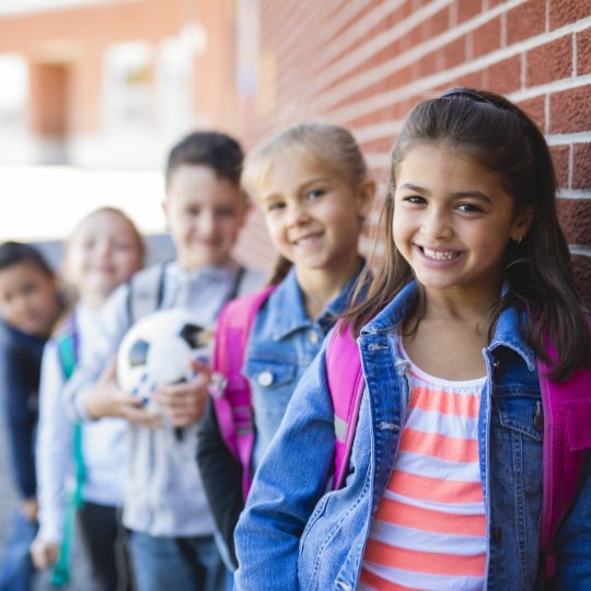 Group of smiling kids with backpacks standing against brick wall