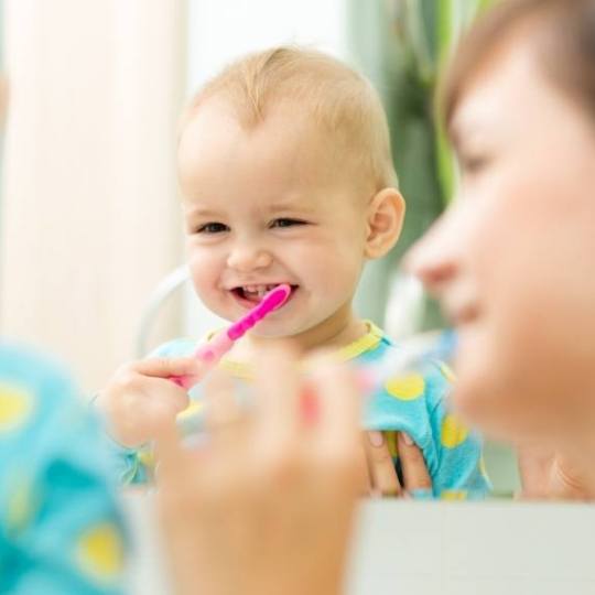 Mother showing toddler how to brush their teeth