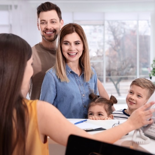 Family of four smiling at dental office receptionist