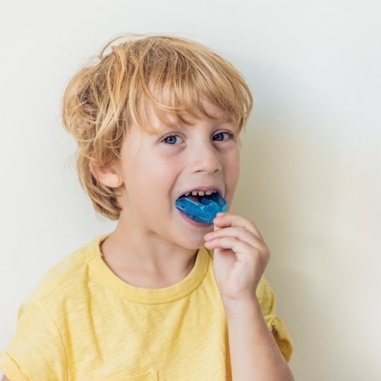 Boy placing blue mouthguard over his teeth