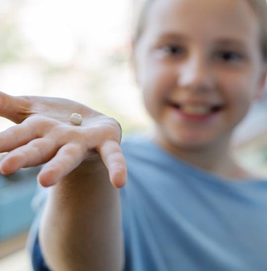 Smiling child holding a tooth after a pediatric tooth extraction