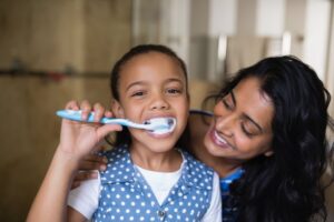 a mother showing her daughter how to brush her teeth